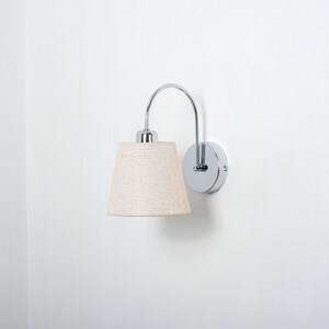 May include: A chrome wall sconce with a curved arm and a beige fabric lampshade.
