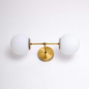 May include: A brass wall sconce with two frosted glass globes. The sconce has a simple, modern design and would be a great addition to any home.