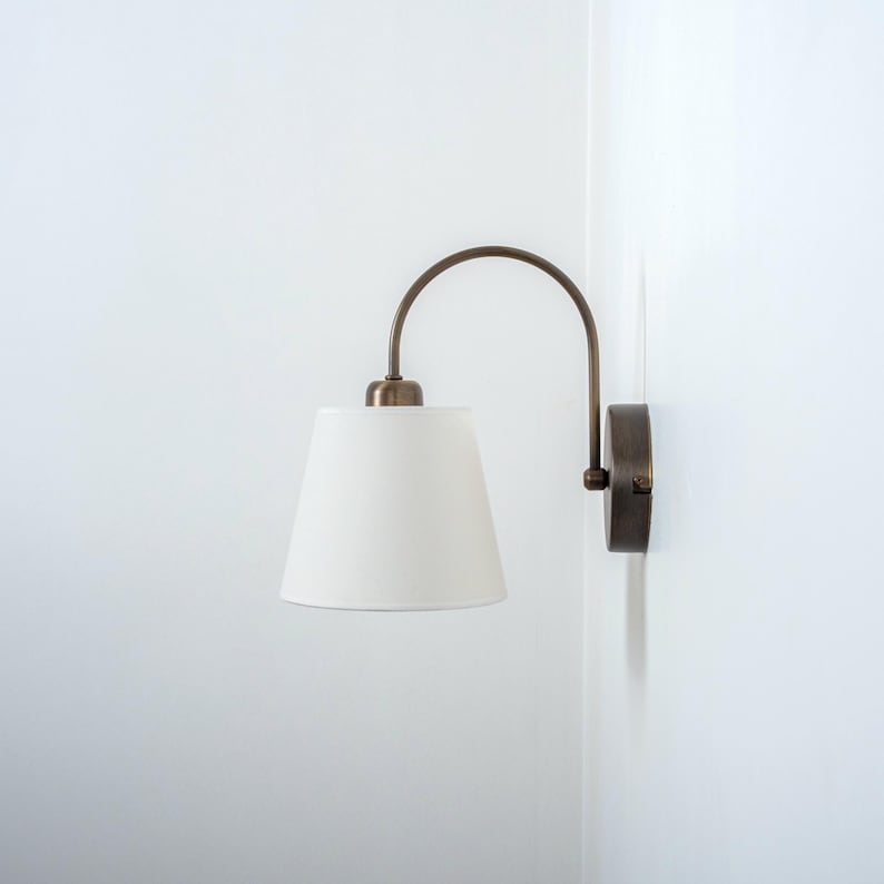 May include: A white wall mounted lamp with a curved arm and a white fabric shade.