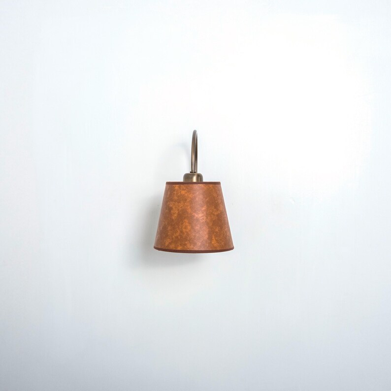 May include: A brown wall sconce with a curved arm and a brown fabric shade.