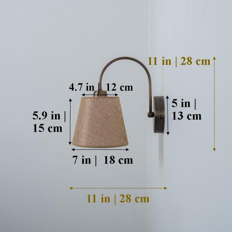 May include: A wall-mounted light fixture with a curved arm and a beige fabric lampshade. The fixture measures 11 inches in height and 5 inches in width. The lampshade is 7 inches in diameter and 4.7 inches in height.