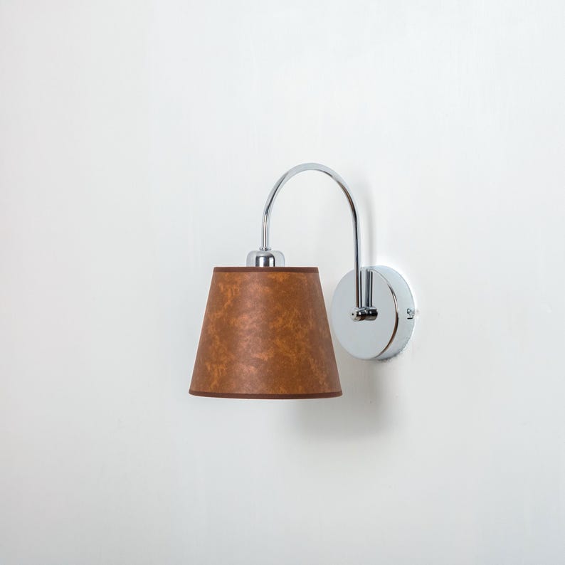 May include: A chrome wall sconce with a brown fabric shade. The sconce has a curved arm and a round base.