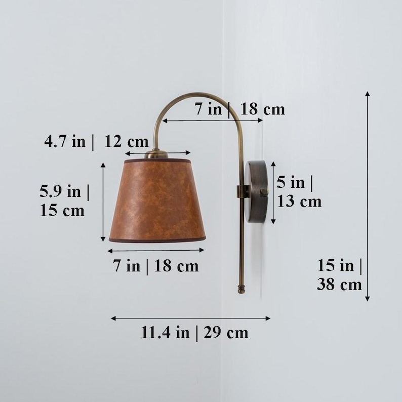 Puede incluir: Una l&aacute;mpara de pared de lat&oacute;n con una pantalla de cuero marr&oacute;n. La l&aacute;mpara mide 38 cm de alto y tiene un brazo de 18 cm. La pantalla tiene un di&aacute;metro de 15 cm y una altura de 12 cm.