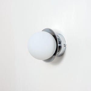May include: A chrome wall sconce with a white frosted glass globe. The sconce has a circular base and a simple design.