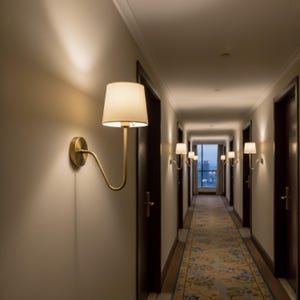 May include: A hallway with several wall-mounted lamps. Each lamp has a gold-colored, curved arm and a cream-colored lampshade. The hallway has dark brown doors and a patterned rug.