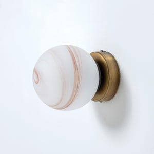 May include: A white glass globe wall sconce with a swirling brown pattern. The sconce has a brass base.