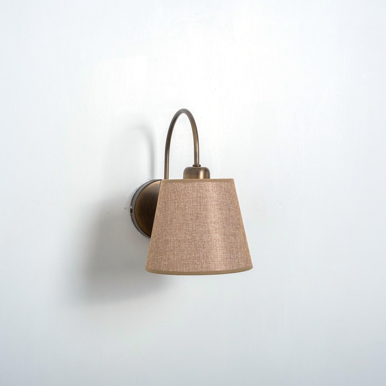 May include: A wall-mounted light fixture with a curved arm and a beige fabric lampshade.