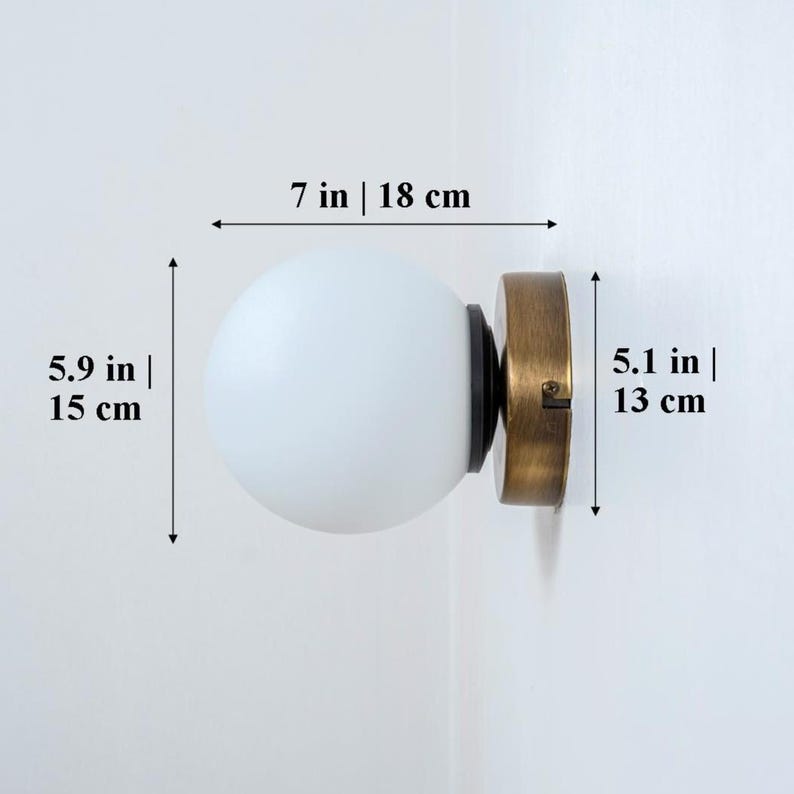 May include: A white frosted glass globe wall sconce with a brass base. The sconce measures 7 inches wide, 5.9 inches tall, and 5.1 inches deep.