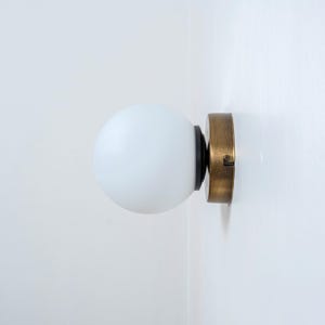 May include: A white frosted glass globe light fixture with a brass base and black accents mounted on a white wall.
