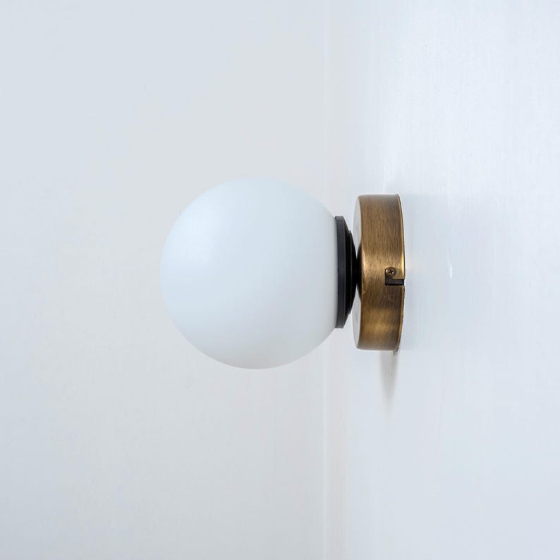 May include: A white frosted glass globe light fixture with a brass base and black accents mounted on a white wall.