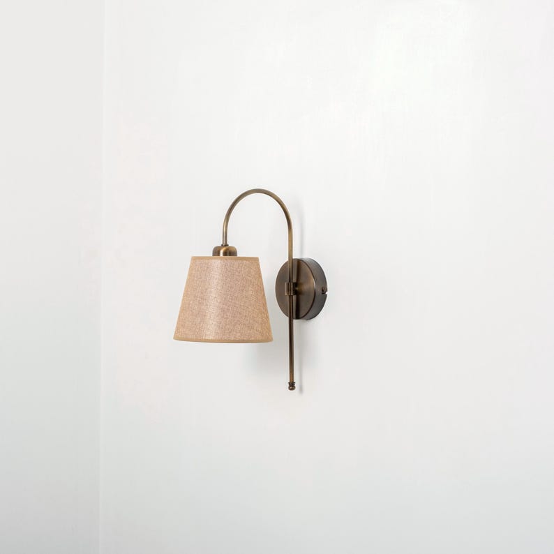 Puede incluir: Una l&aacute;mpara de pared con un brazo curvo y una pantalla de tela beige. La l&aacute;mpara est&aacute; acabada en lat&oacute;n cepillado.