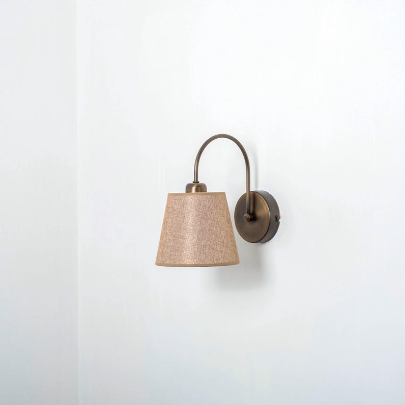 May include: A wall-mounted light fixture with a curved arm and a beige fabric lampshade.