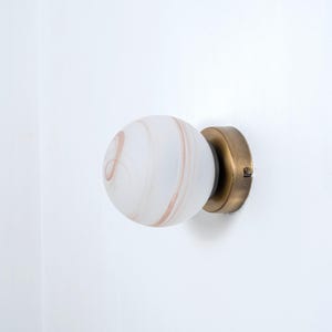 May include: A brass wall sconce with a white globe-shaped light fixture. The globe has a swirling, marbled pattern in shades of brown and white.