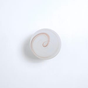 May include: A white glass paperweight with a swirling brown design.