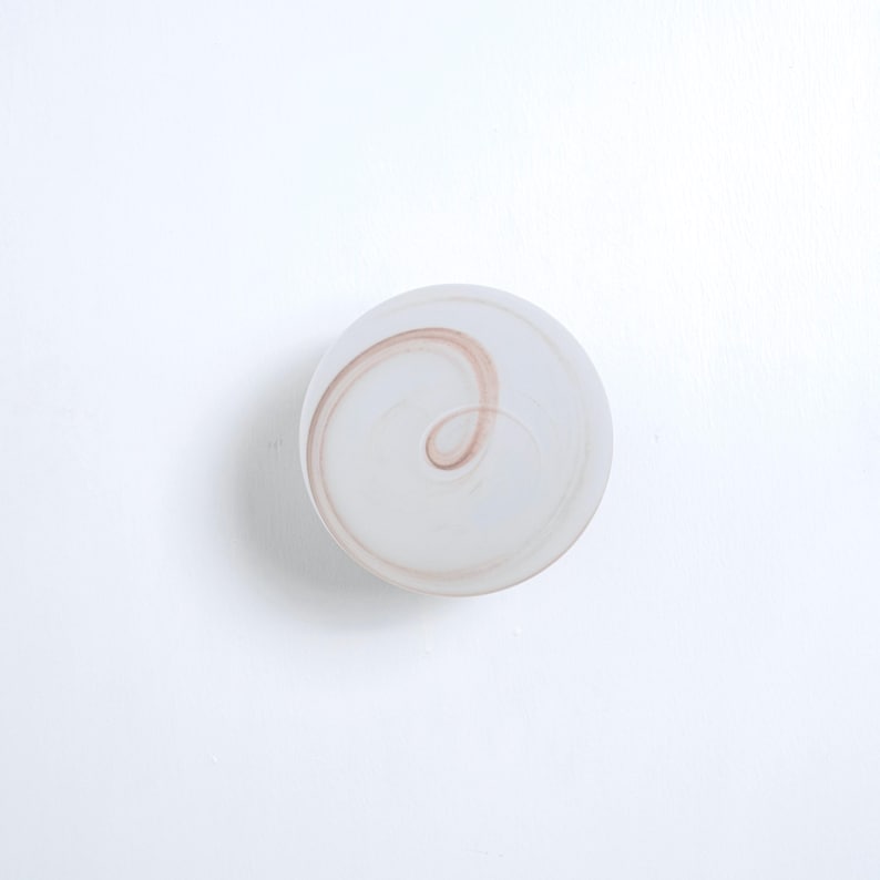 May include: A white glass paperweight with a swirling brown design.