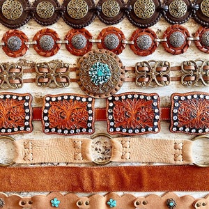 K&ouml;nnte beinhalten: Eine Sammlung von acht Lederg&uuml;rteln mit verschiedenen Designs und Verzierungen. Die G&uuml;rtel sind in verschiedenen Farben gehalten, darunter Braun, Beige und T&uuml;rkis. Einige G&uuml;rtel haben komplizierte Muster, w&auml;hrend andere schlichte Designs haben. Die G&uuml;rtel sind in einer Reihe angeordnet, wobei der aufwendigste G&uuml;rtel oben und der einfachste G&uuml;rtel unten liegt.