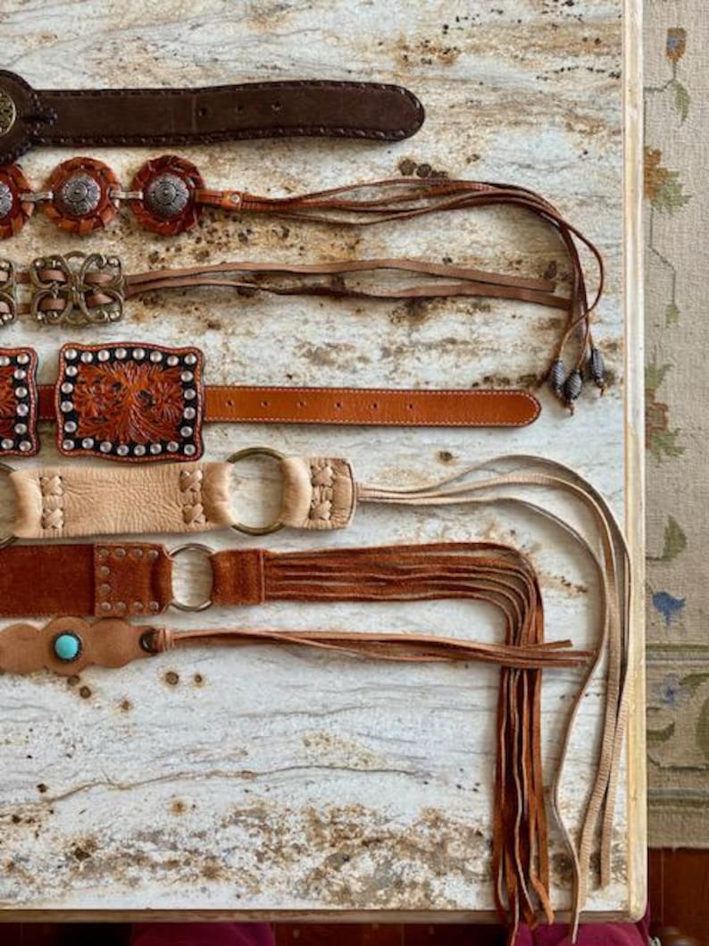 K&ouml;nnte beinhalten: F&uuml;nf Lederg&uuml;rtel mit Fransen. Die G&uuml;rtel sind braun, beige und sandfarben. Einige G&uuml;rtel haben Metallschnallen und dekorative N&auml;hte.