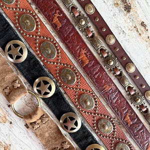 Peut inclure: Cinq ceintures en cuir diff&eacute;rentes avec divers ornements m&eacute;talliques. Les ceintures pr&eacute;sentent diff&eacute;rents motifs, notamment des &eacute;toiles, des cercles et des motifs animaliers. Les ceintures sont toutes brunes et ont un style rustique et western.