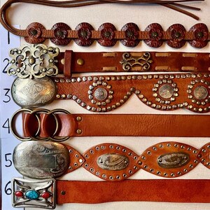 May include: Six different brown leather belts with various metal accents and embellishments. The belts have different styles of buckles, including a silver oval buckle with a turquoise stone, a silver oval buckle with a floral design, and a silver buckle with a geometric design.