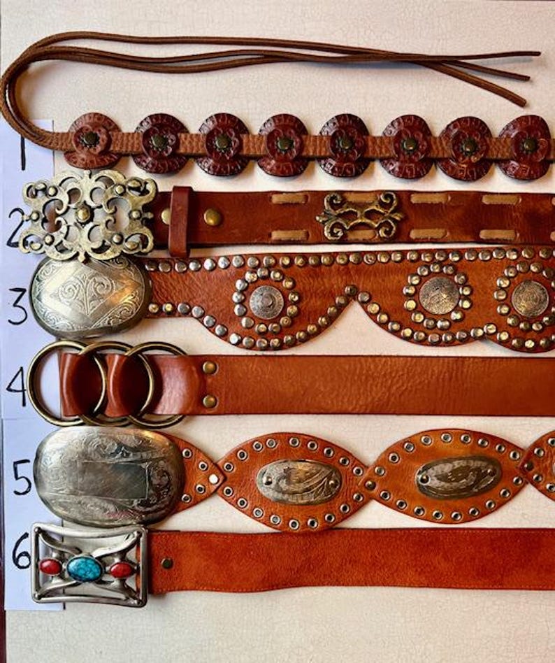 May include: Six different brown leather belts with various metal accents and embellishments. The belts have different styles of buckles, including a silver oval buckle with a turquoise stone, a silver oval buckle with a floral design, and a silver buckle with a geometric design.
