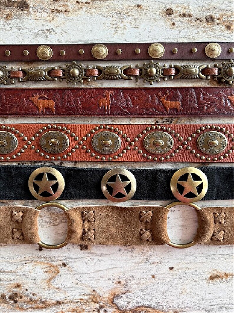 Peut inclure: Cinq ceintures en cuir diff&eacute;rentes avec divers accents m&eacute;talliques. Les ceintures pr&eacute;sentent diff&eacute;rents motifs, notamment des &eacute;toiles, des cercles et des motifs animaliers. Les ceintures sont dispos&eacute;es en pile, la ceinture du haut &eacute;tant brune et la ceinture du bas &eacute;tant beige.