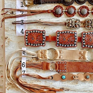 K&ouml;nnte beinhalten: Sieben verschiedene Lederg&uuml;rtel mit verschiedenen Verzierungen, darunter Fransen, Nieten und Metallakzente. Die G&uuml;rtel sind von 1 bis 7 nummeriert.