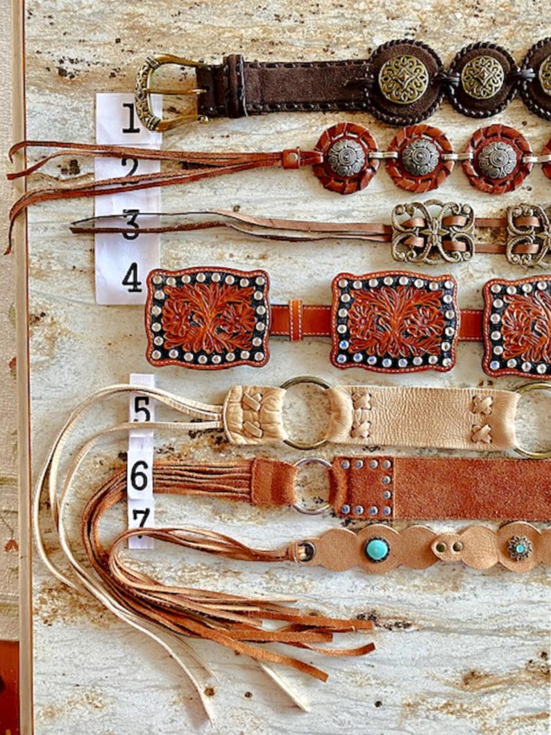K&ouml;nnte beinhalten: Sieben verschiedene Lederg&uuml;rtel mit verschiedenen Verzierungen, darunter Fransen, Nieten und Metallakzente. Die G&uuml;rtel sind von 1 bis 7 nummeriert.
