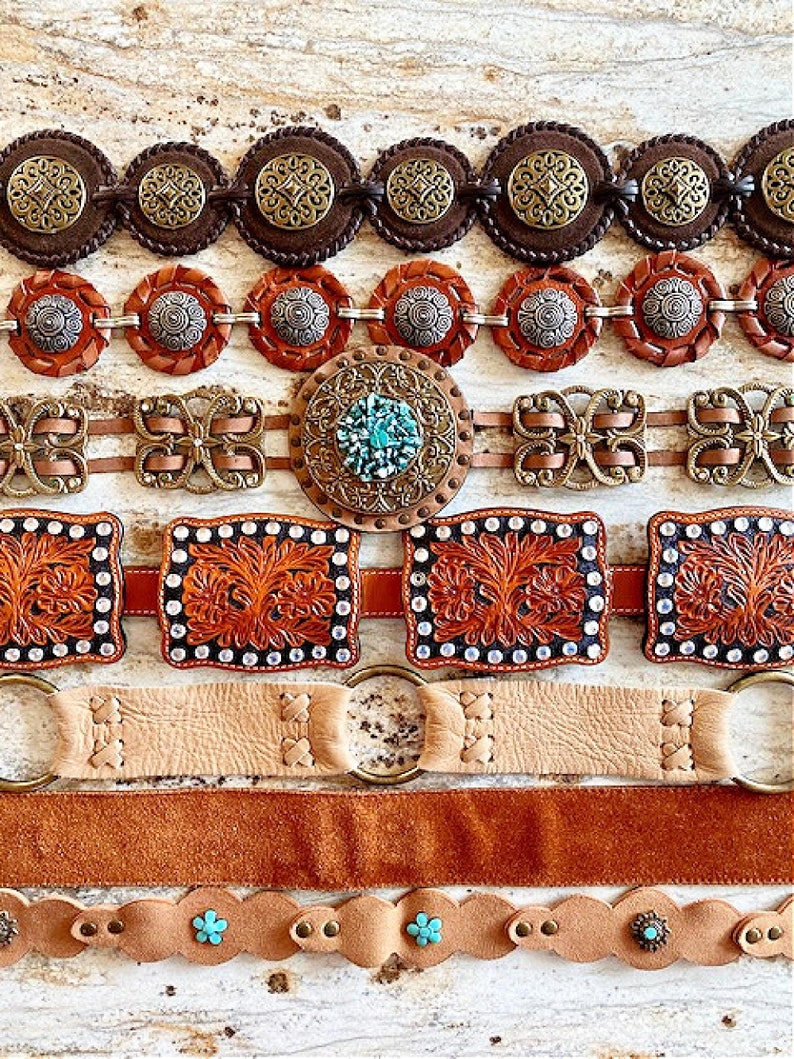 K&ouml;nnte beinhalten: Eine Sammlung von acht Lederg&uuml;rteln mit verschiedenen Designs und Verzierungen. Die G&uuml;rtel sind in verschiedenen Farben gehalten, darunter Braun, Beige und T&uuml;rkis. Einige G&uuml;rtel haben komplizierte Muster, w&auml;hrend andere schlichte Designs haben. Die G&uuml;rtel sind in einer Reihe angeordnet, wobei der aufwendigste G&uuml;rtel oben und der einfachste G&uuml;rtel unten liegt.