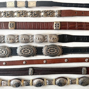 May include: A collection of vintage belts with various designs. The belts feature different colors, including black, brown, and tan. Buckles and decorative elements are silver and gold-toned, with intricate patterns and textures. Styles include braided, embossed, and studded.