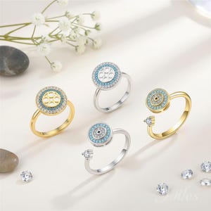 May include: Four rings with a central circular design, each featuring a different color scheme. Two rings are gold-toned, and two are silver-toned. The central design is surrounded by small, sparkling stones. One ring has a small, additional stone on the band.
