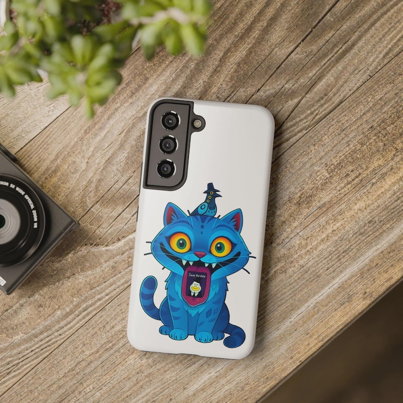 May include: A white phone case featuring a cartoon blue cat with large yellow eyes and a bird on its head. The cat has a wide grin, and its tongue displays a small graphic with the text "Save the Milk". The case has a black camera module.