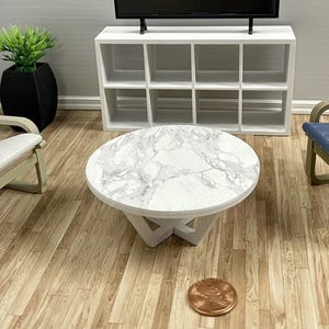 May include: White round coffee table with a marble top and a white, geometric base. The table is sitting on a wooden floor.