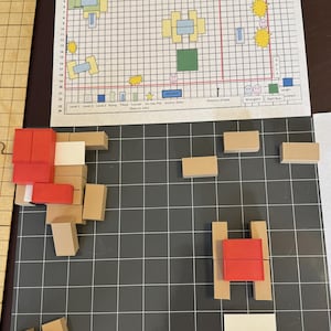 May include: A dog agility course game board with a grid pattern. The board includes a printed map with various obstacles and the word "START". Wooden blocks in red and tan are arranged on the board, representing course elements.