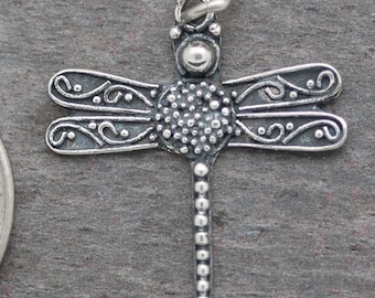 Könnte beinhalten: Silberner Libellen-Anhänger mit filigranen Details und einer perlenbesetzten Schwanzflosse. Die Flügel der Libelle sind gekrümmt und haben ein zartes Design.