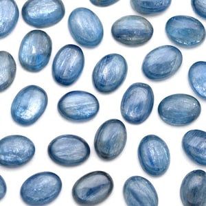 May include: A collection of oval-shaped blue kyanite stones, each with a unique striated pattern. The stones are smooth and polished, with a light blue color.