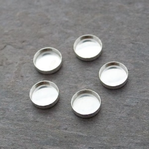 Può includere: Cinque basi rotonde in metallo color argento per la creazione di gioielli. Le basi sono lisce e hanno una finitura lucida.