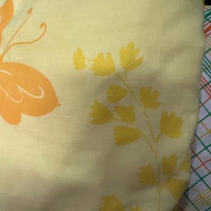 May include: A yellow fabric with a floral pattern. The flowers are yellow and orange and have a simple, stylized design.