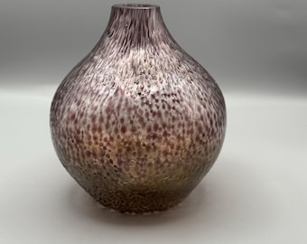 May include: A decorative glass vase with a bulbous body and a narrow neck. The vase has a speckled texture with shades of purple, brown, and gold. The glass appears to have a metallic sheen, adding to its visual appeal.