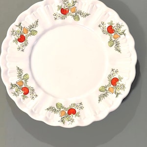 May include: White ceramic plate with a scalloped edge and a floral design featuring red tomatoes, green leaves, and yellow flowers.