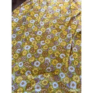 Puede incluir: Una tela con un patrón floral repetido. Las flores son en tonos de amarillo, blanco, marrón y morado, sobre un fondo amarillo-verdoso. La tela parece ser un textil vintage, posiblemente para ropa o decoración del hogar.
