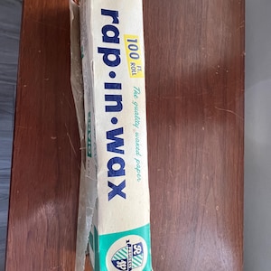 Könnte beinhalten: Eine Vintage-Schachtel Rap-In-Wax Wachspapier in einer 30,5 Meter Rolle. Die Schachtel ist weiß mit grünen und blauen Akzenten und zeigt ein Schildlogo mit dem Text "R Protects".
