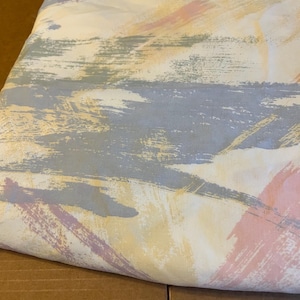 May include: A white fabric with a colourful abstract pattern. The pattern features brushstrokes in shades of pink, yellow, blue, and green.