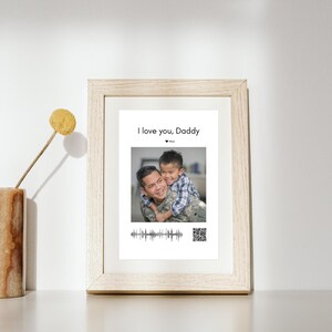 May include: A framed photo with a father and son. The son is giving his father a hug from behind. The photo has the text "I love you, Daddy" and a heart with the word "Max". There is a sound wave and a QR code below the photo.