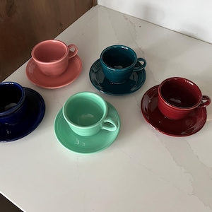 May include: Five teacups and saucers in different colors, including blue, green, red, and pink. The cups and saucers are all the same size and shape.