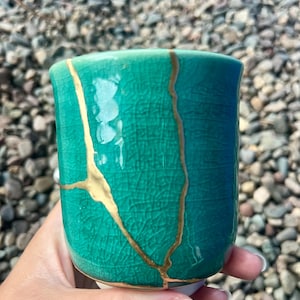 May include: A teal ceramic mug with gold crackle glaze. The mug has a unique, hand-crafted look.