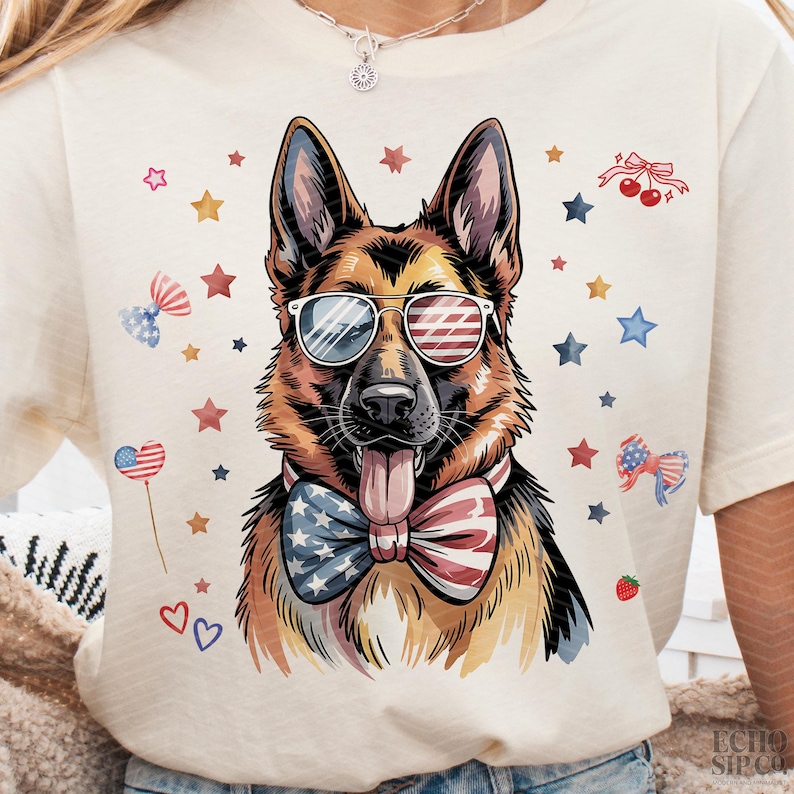 May include: Cream-coloured t-shirt featuring a German Shepherd wearing sunglasses with an American flag design and a patriotic bow tie. The design includes red, white, and blue stars, bows, and hearts, celebrating Independence Day.