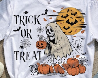 Op de afbeelding: Wit T-shirt met een Halloween-thema. Het ontwerp toont een skelet met een pompoen, omringd door pompoenen, vleermuizen, spinnenwebben en de woorden "Trick or Treat". Op de achtergrond is een volle maan te zien.