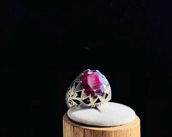 May include: A silver ring with a large, oval-shaped, deep red gemstone set in a detailed, ornate design.