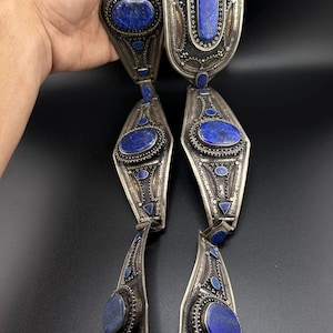 Op de afbeelding: Een zilveren ketting met meerdere lapis lazuli-stenen die zijn gezet in ingewikkeld zilverwerk. De ketting bestaat uit verschillende verbonden secties, elk met een grote ovale lapis lazuli-steen omgeven door kleinere stenen en gedetailleerde zilveren ontwerpen.