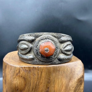 Può includere: Un braccialetto d'argento con intricati disegni incisi e una grande pietra arancione al centro.
